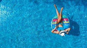 Aerial view of beautiful girl in swimming pool from above, swim on inflatable ring donut and has fun in water on family vacation