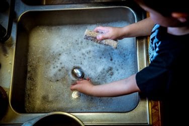 child washes dishes at the kitchen sink