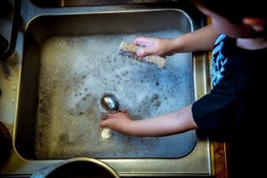 child washes dishes at the kitchen sink